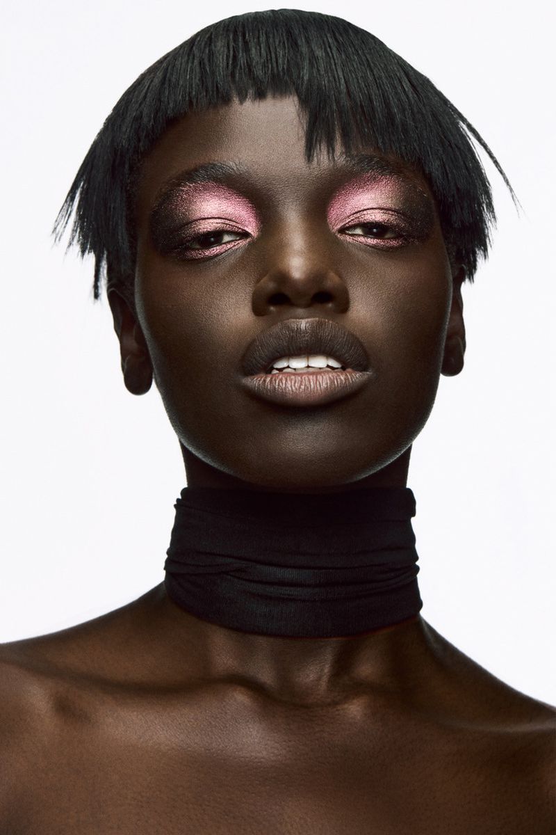 Close-up portrait of an African-American female with short black hair and pink eye shadow, wearing a black fabric choker against a white backdrop.