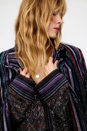 Model with long blonde hair wearing a patterned striped jacket against a neutral studio background