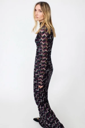 Model wearing a long-sleeved patterned chevron dress standing against a plain white background.