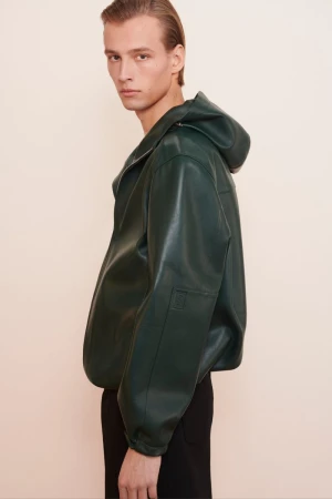 Model wearing a dark green hooded leather jacket against a light neutral background