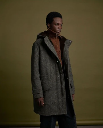 Model in grey hooded wool coat and brown turtleneck against an olive green seamless background for Yves Salomon