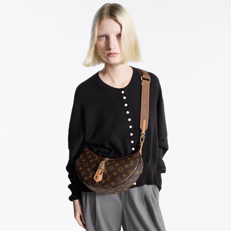 A blonde model presents a Louis Vuitton bag with a brown strap, wearing a black cardigan, against a bright white background in a studio shot.