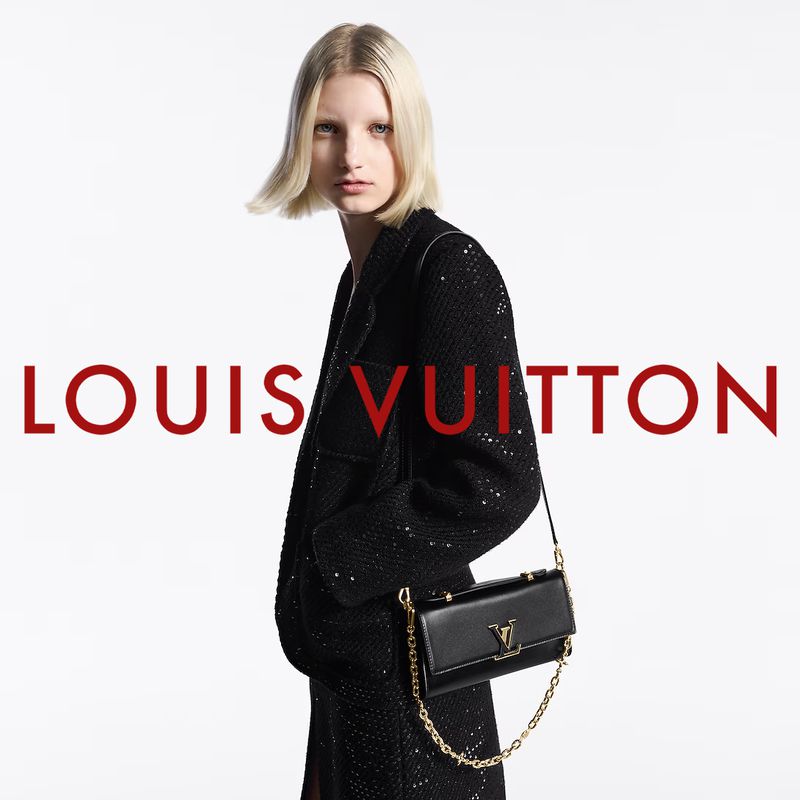 Fashion shot: a blonde model in a sequined jacket poses with a Louis Vuitton bag against a white backdrop, showcasing luxury and style.