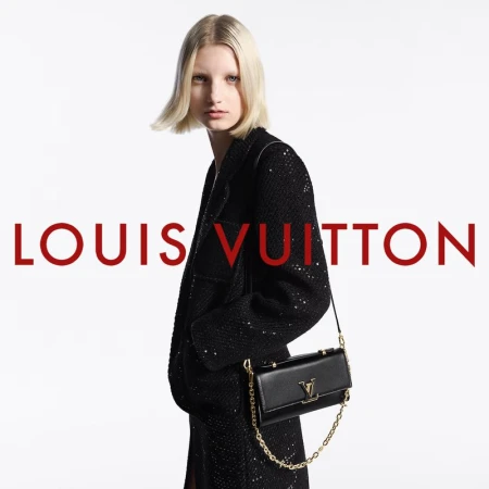 Fashion shot: a blonde model in a sequined jacket poses with a Louis Vuitton bag against a white backdrop, showcasing luxury and style.