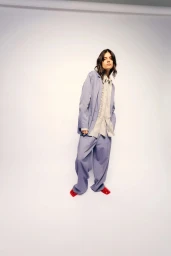 Model standing in a relaxed pose wearing a light blue oversized suit and red shoes against a white backdrop.