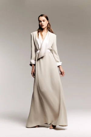 Full-length shot of a female fashion model in a light tan gown with white trim against a neutral grey studio backdrop, minimalist fashion.