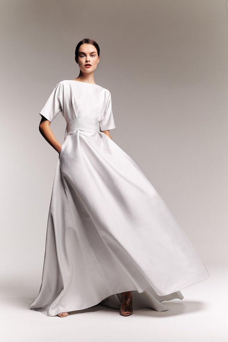 Model in a white short-sleeve midi dress standing against a plain gradient background for Alexis Mabille lookbook.