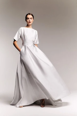 Model in a white short-sleeve midi dress standing against a plain gradient background for Alexis Mabille lookbook.