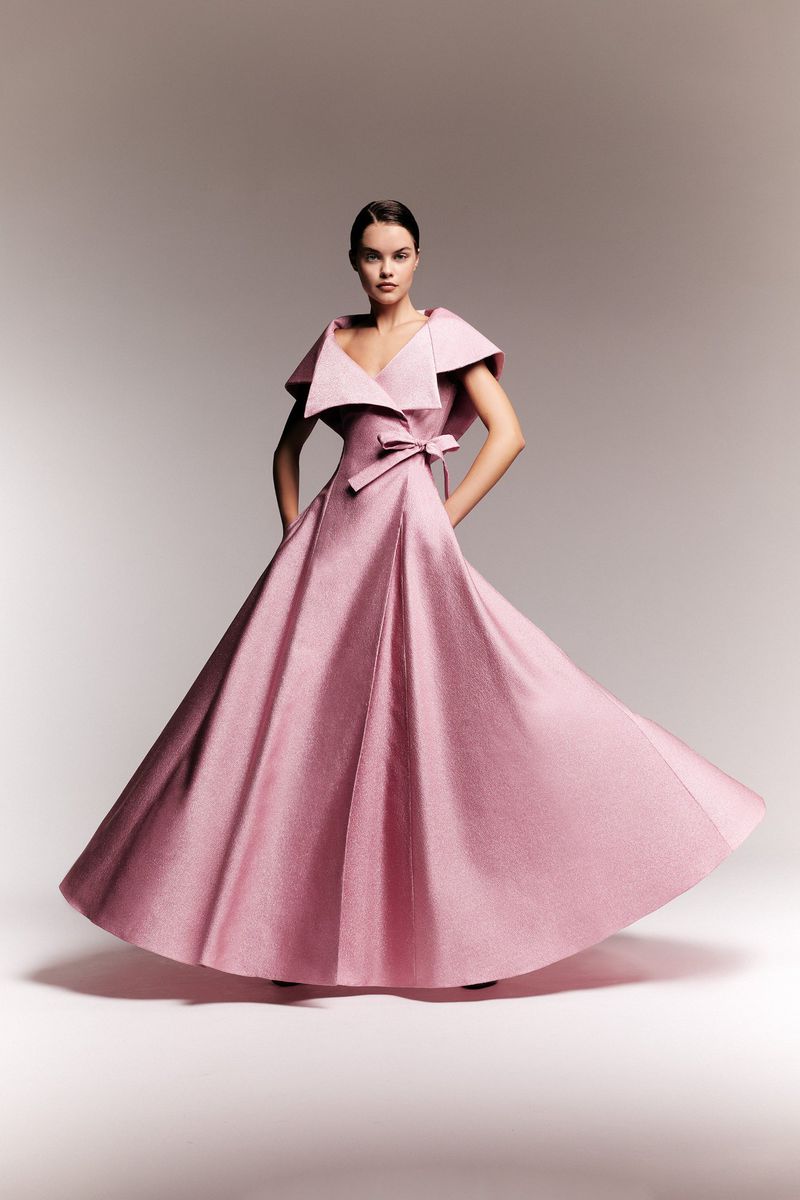 Woman in pink ballgown with bow posing in photo studio with soft lighting. Elegant couture dress and formal fashion portrait.