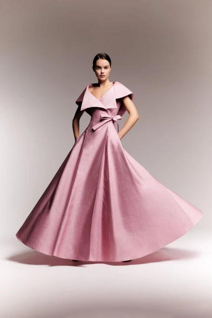 Woman in pink ballgown with bow posing in photo studio with soft lighting. Elegant couture dress and formal fashion portrait.