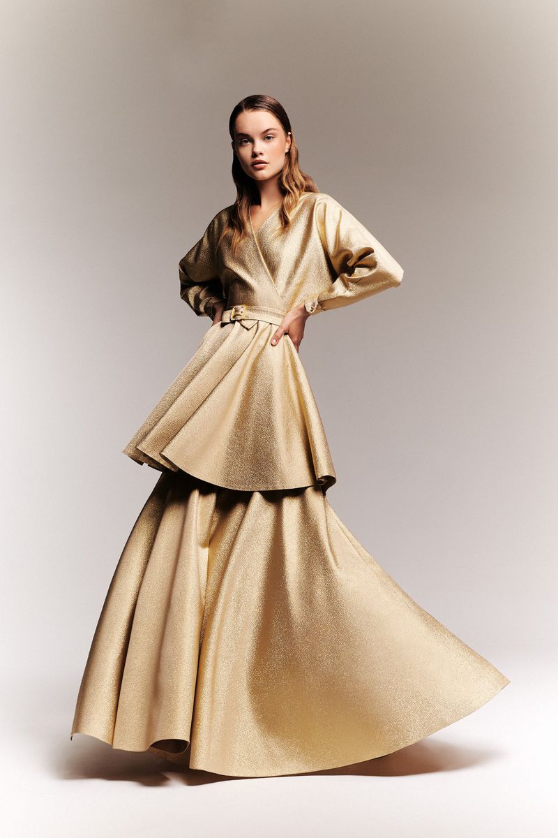Model in a metallic gold belted wrap top and matching flared maxi skirt posing against a neutral studio backdrop.