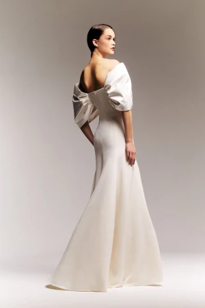 Model in off-the-shoulder white gown posing against a grey studio backdrop for Alexis Mabille ready-to-wear lookbook