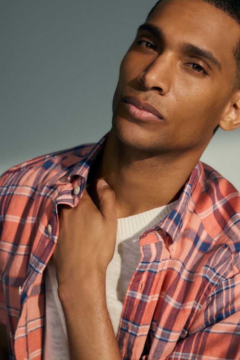 Close-up studio portrait of a handsome adult male model with tan skin, wearing a red and blue plaid shirt and a white t-shirt.
