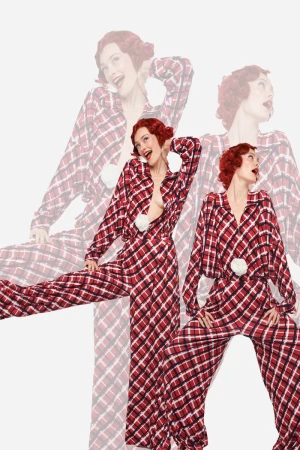 Adult female fashion model wearing plaid pajama set with flower accent poses in a studio with red hair and fair skin.