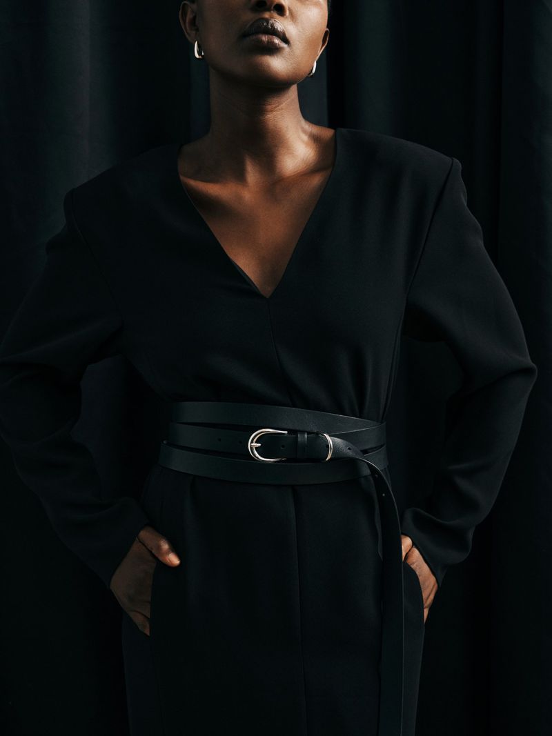 Portrait of an African American woman in a dark top with a black belt, posing against a dark curtain backdrop in a studio setting.
