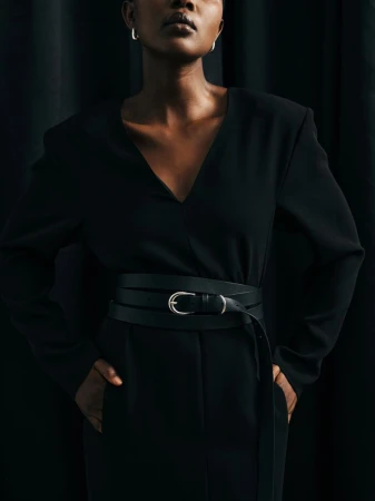 Portrait of an African American woman in a dark top with a black belt, posing against a dark curtain backdrop in a studio setting.