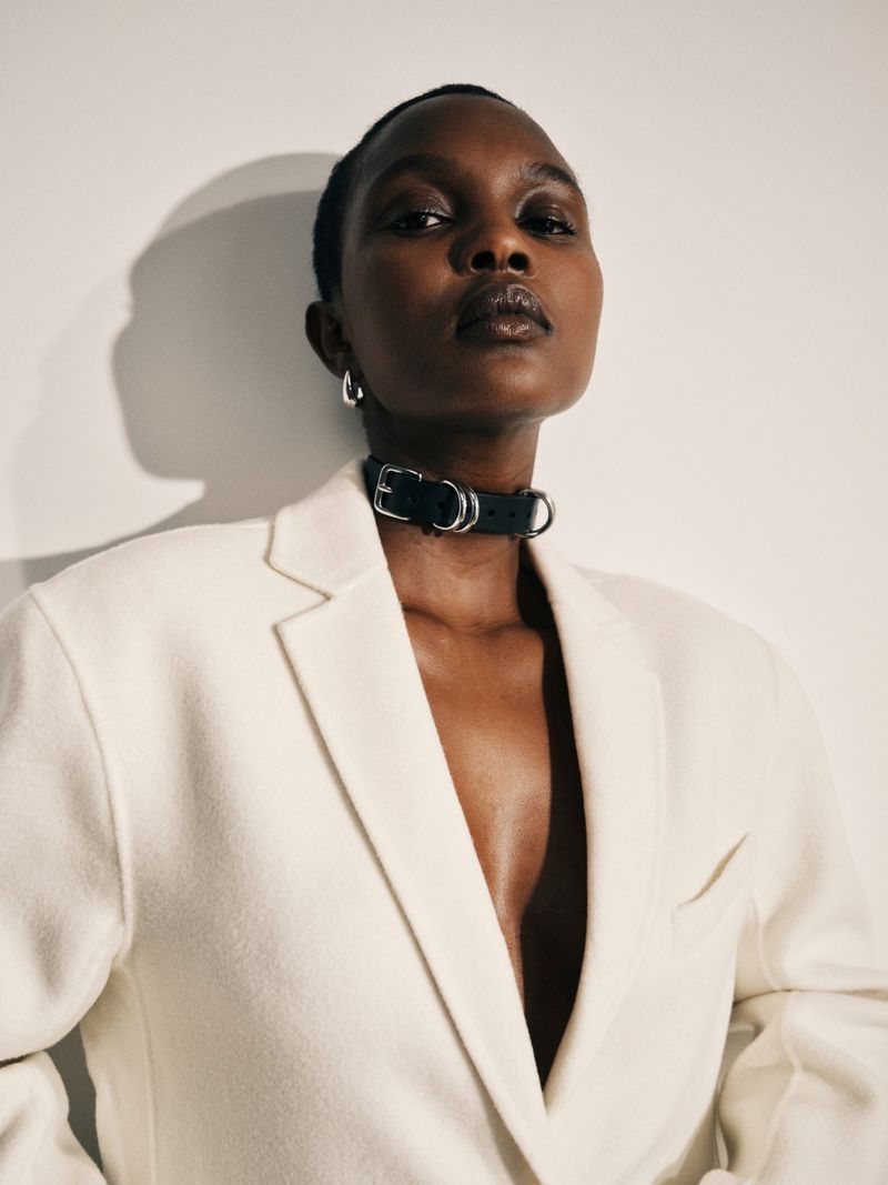 Headshot of an African woman wearing a white blazer and black choker. Portrait on a clean white background, neutral expression, fashion shot.