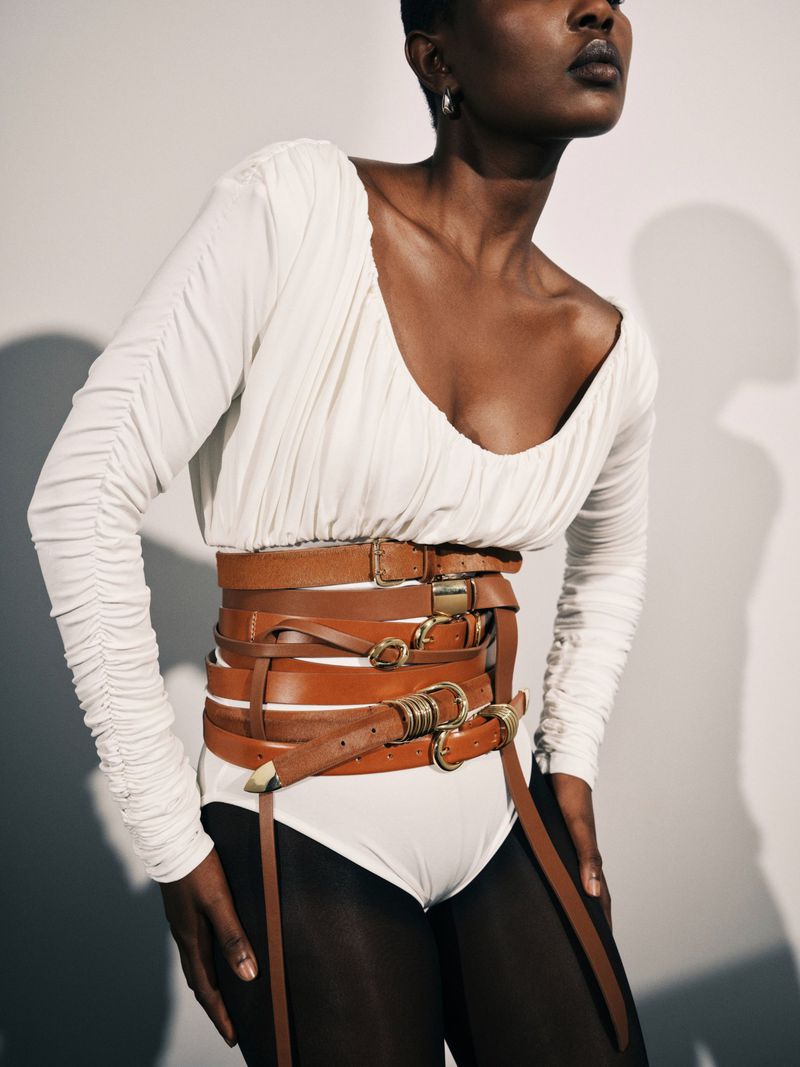 Woman in white bodysuit with oversized leather belt corset fashion in studio. Tights and long sleeve top. Editorial fashion shot.