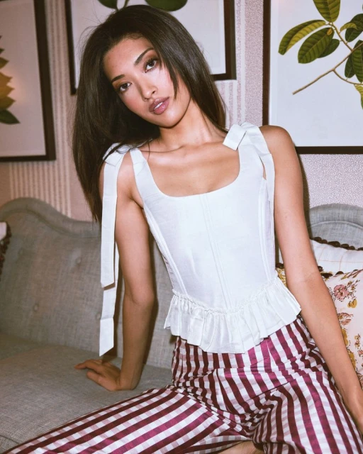 Portrait of an adult female in a white top and red striped pants, sitting on a couch, with framed artwork in the background.