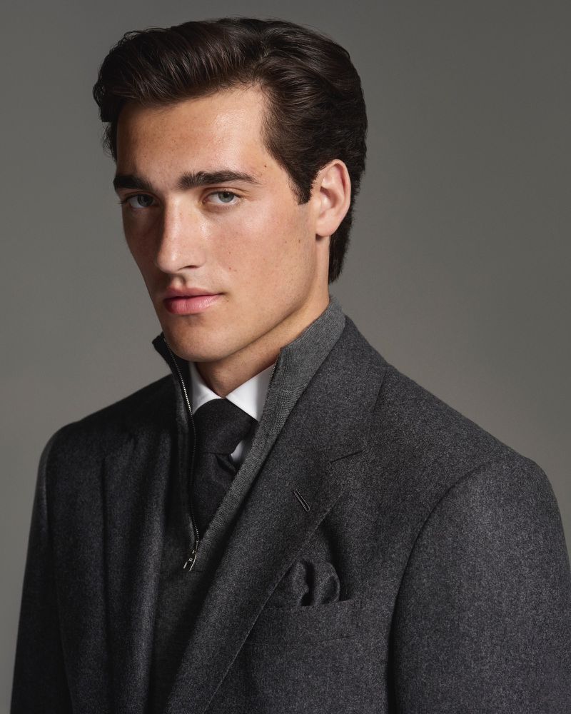 Portrait of a handsome adult male with dark hair, wearing a gray suit jacket, vest, and tie, posing in a photo studio setting.