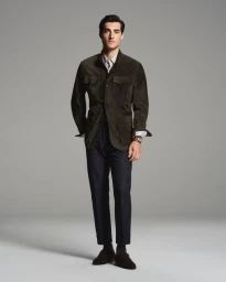 Full-length portrait of a male model wearing an olive field jacket and dark trousers against a grey studio background