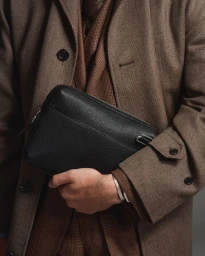 Man wearing a brown wool coat and houndstooth suit holding a black leather pouch bag