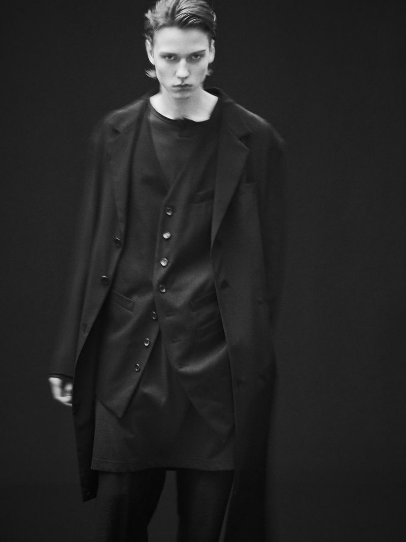 Young male model wearing a black suit jacket and vest against a dark seamless background