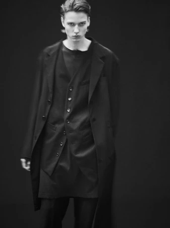 Young male model wearing a black suit jacket and vest against a dark seamless background