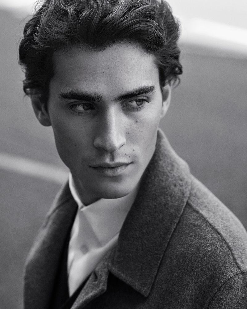 Black and white portrait of a young man in a wool coat looking off-camera with soft, diffused lighting and a shallow depth of field.