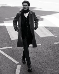 Man wearing a grey wool coat and scarf walking on an asphalt street with road markings.