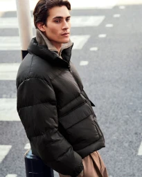 Model wearing a black puffer jacket outdoors on a city street for COS menswear campaign