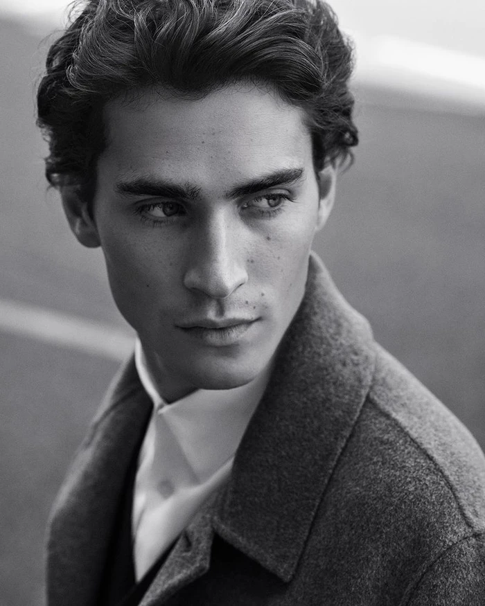 Close-up black and white portrait of a male model wearing a collared shirt and dark outerwear piece.