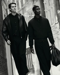 Two male models in dark outerwear walking down an urban street for COS menswear campaign