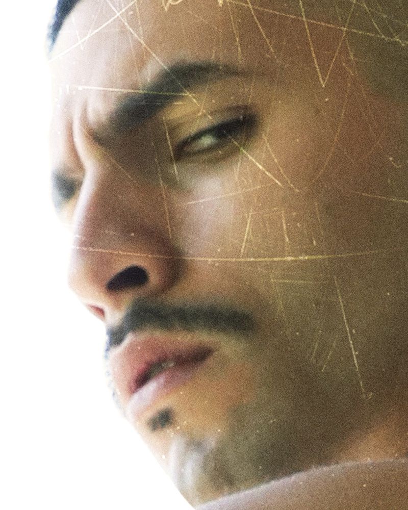Close-up portrait of a man looking at the camera with a serious expression and gold line effects overlaying his face in a dramatic way.