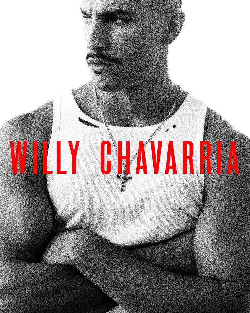 Black and white portrait of an adult male with arms crossed, wearing a white tank top and a cross necklace, against a white backdrop.
