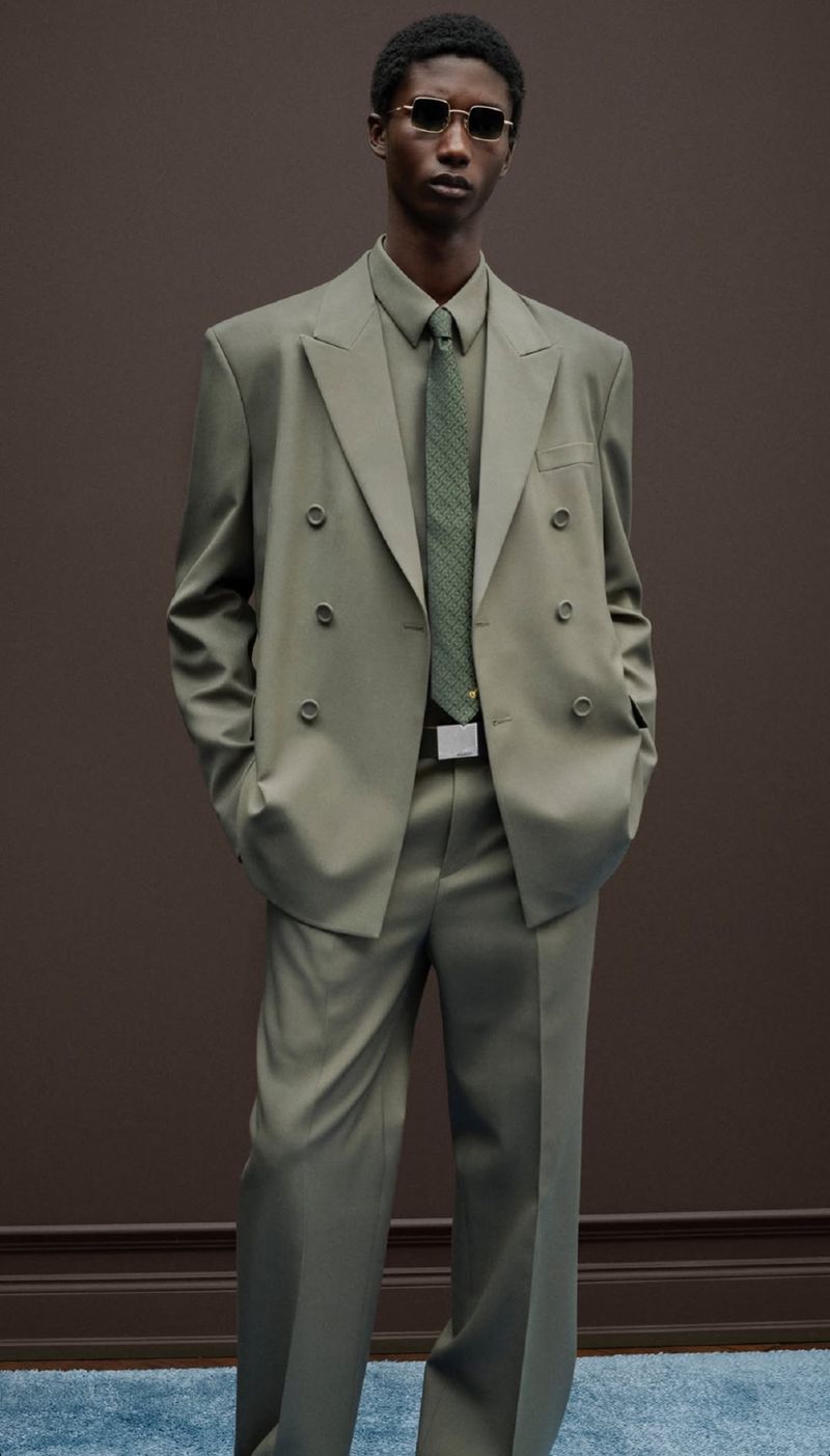 Studio shot of an African-American male model in an olive green double-breasted suit and sunglasses, striking a confident pose.