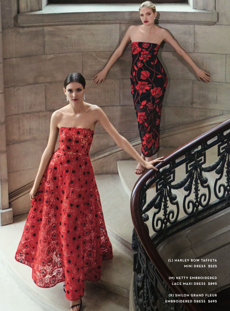 Two adult women pose on a staircase in red and black floral strapless evening gowns, marble stone wall background.