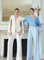 Two female models posing in front of a white fireplace wearing white cape blazer suit and light blue feather-cuff sweater