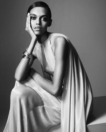 Elegant black and white portrait of a woman in a flowing dress, seated with her hand to her face in a thoughtful pose.