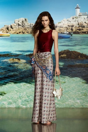 Young woman posing in a maroon top and long printed skirt on a beach with a lighthouse in the background. Fashion shot.