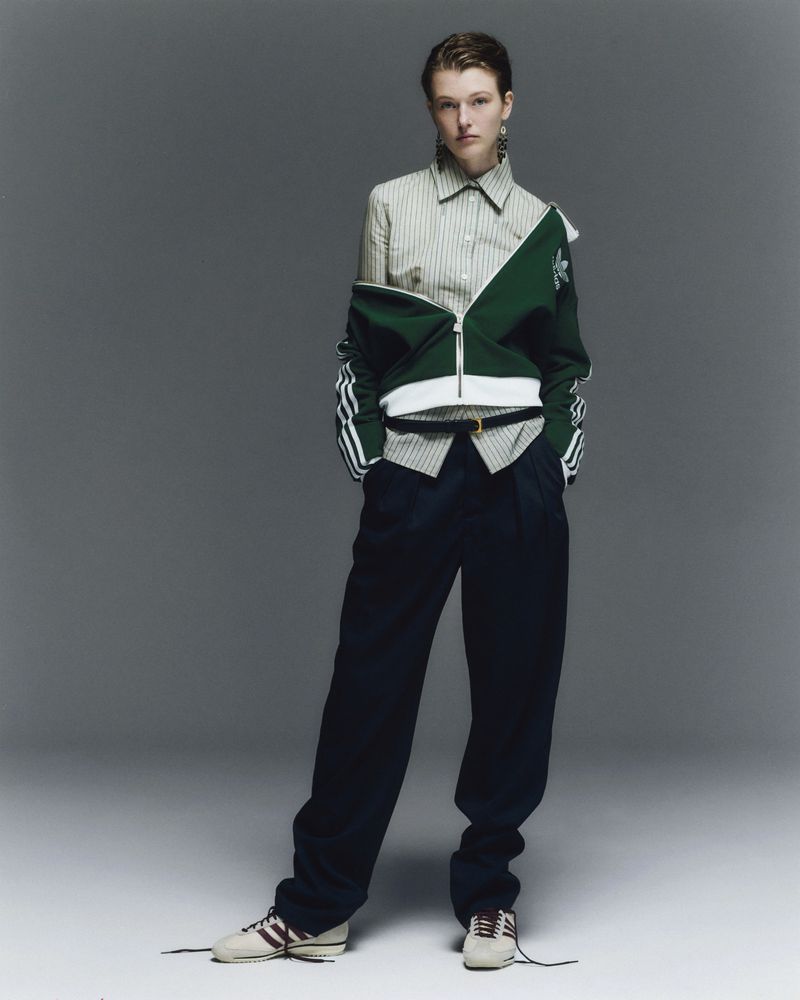 Woman in striped shirt, green jacket, and navy pants poses in studio. Fashion editorial shot with neutral backdrop and natural lighting.