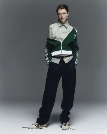 Woman in striped shirt, green jacket, and navy pants poses in studio. Fashion editorial shot with neutral backdrop and natural lighting.