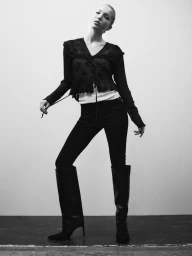 Model Lila Moss in dark clothing and tall boots against a plain white studio background for Zara Denim.