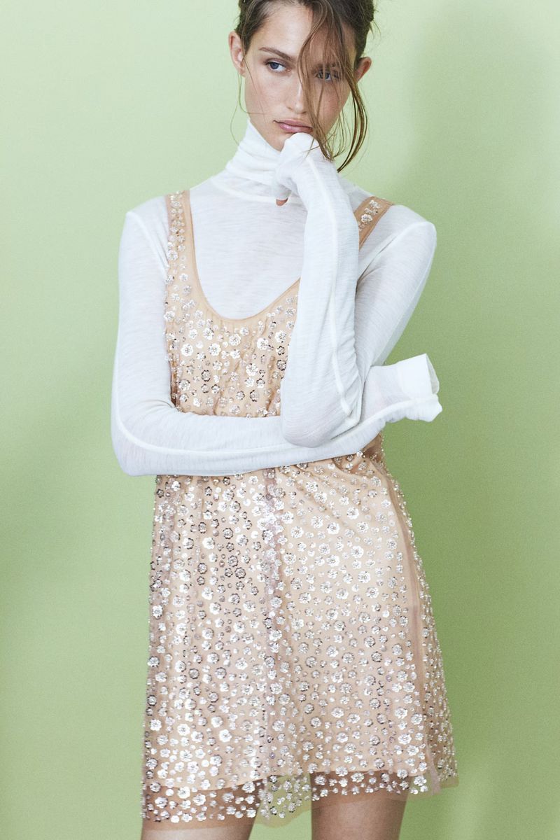 Model Vika Evseeva in a white turtleneck and sequin dress against a pale green background for H&M