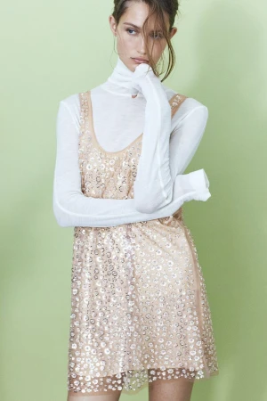 Model Vika Evseeva in a white turtleneck and sequin dress against a pale green background for H&M