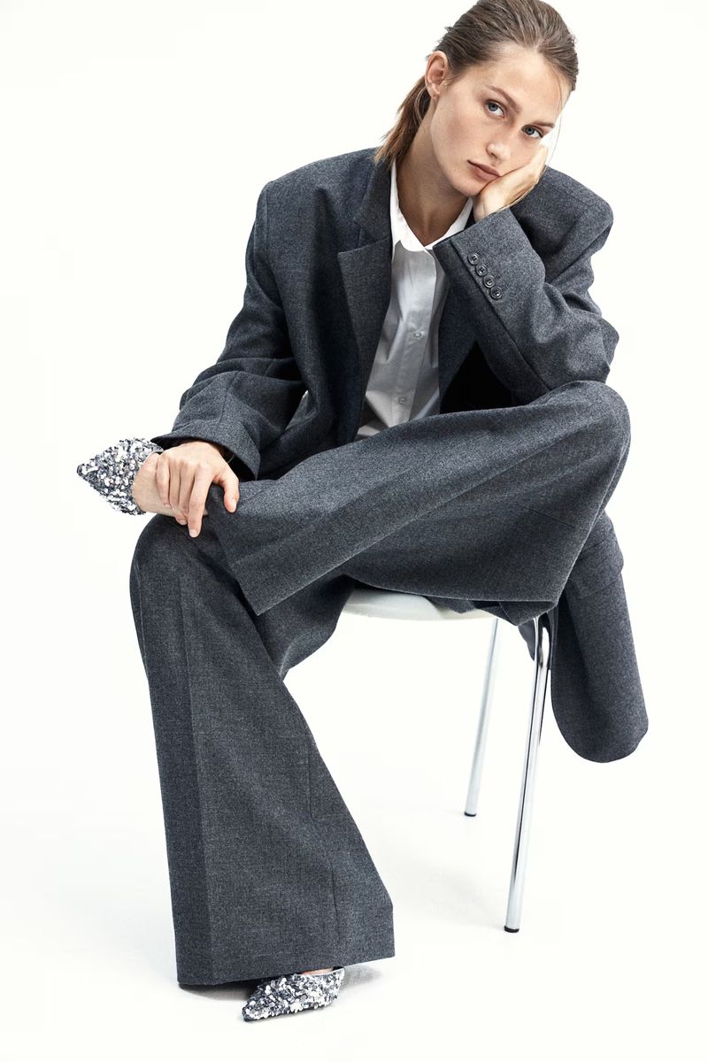 Model Vika Evseeva in an oversized grey suit seated on a white chair against a white background for H&M Woman Oyster