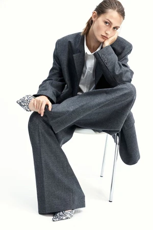 Model Vika Evseeva in an oversized grey suit seated on a white chair against a white background for H&M Woman Oyster