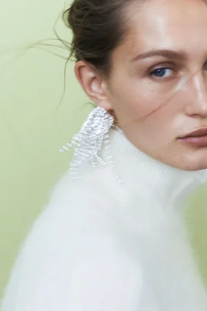 Close-up portrait of Vika Evseeva wearing a white turtleneck and large silver statement earrings against a light background.