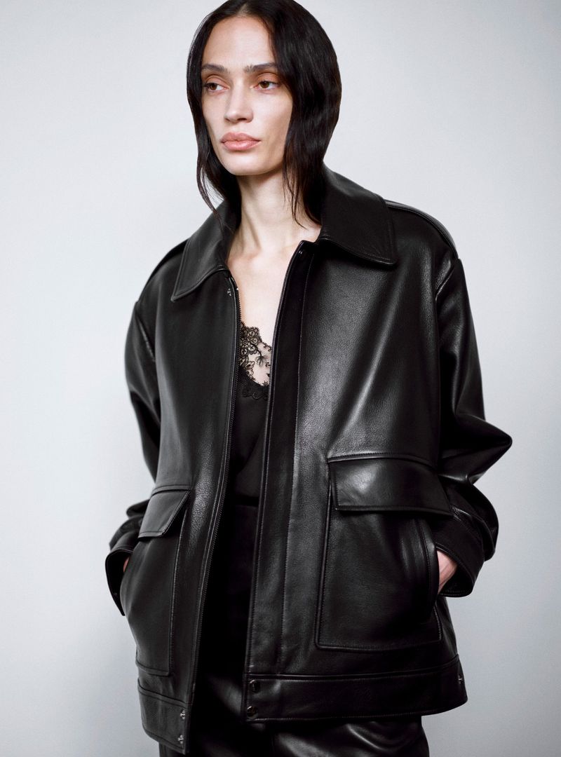 Model wearing a black leather jacket with front pockets against a pale grey background for Nour Hammour Resort 25