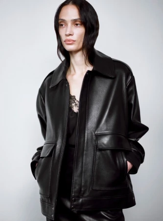 Model wearing a black leather jacket with front pockets against a pale grey background for Nour Hammour Resort 25
